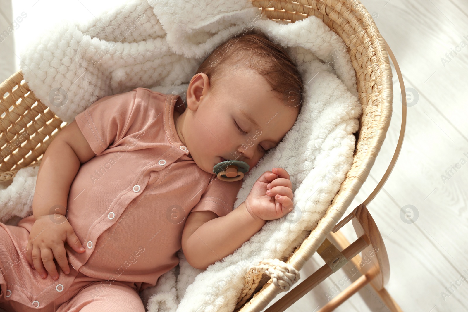 Photo of Cute little baby with pacifier sleeping in wicker crib at home, above view