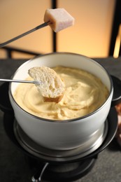 Photo of Forks with pieces of ham and bread over fondue pot with melted cheese on grey table, closeup