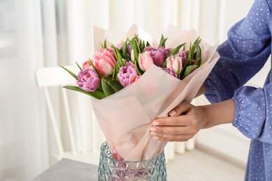 Photo of Woman putting bouquet of beautiful tulips in vase indoors, closeup