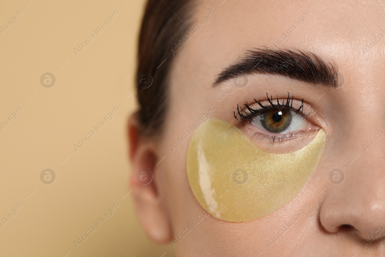 Photo of Beautiful woman with under eye patch on beige background, closeup. Space for text