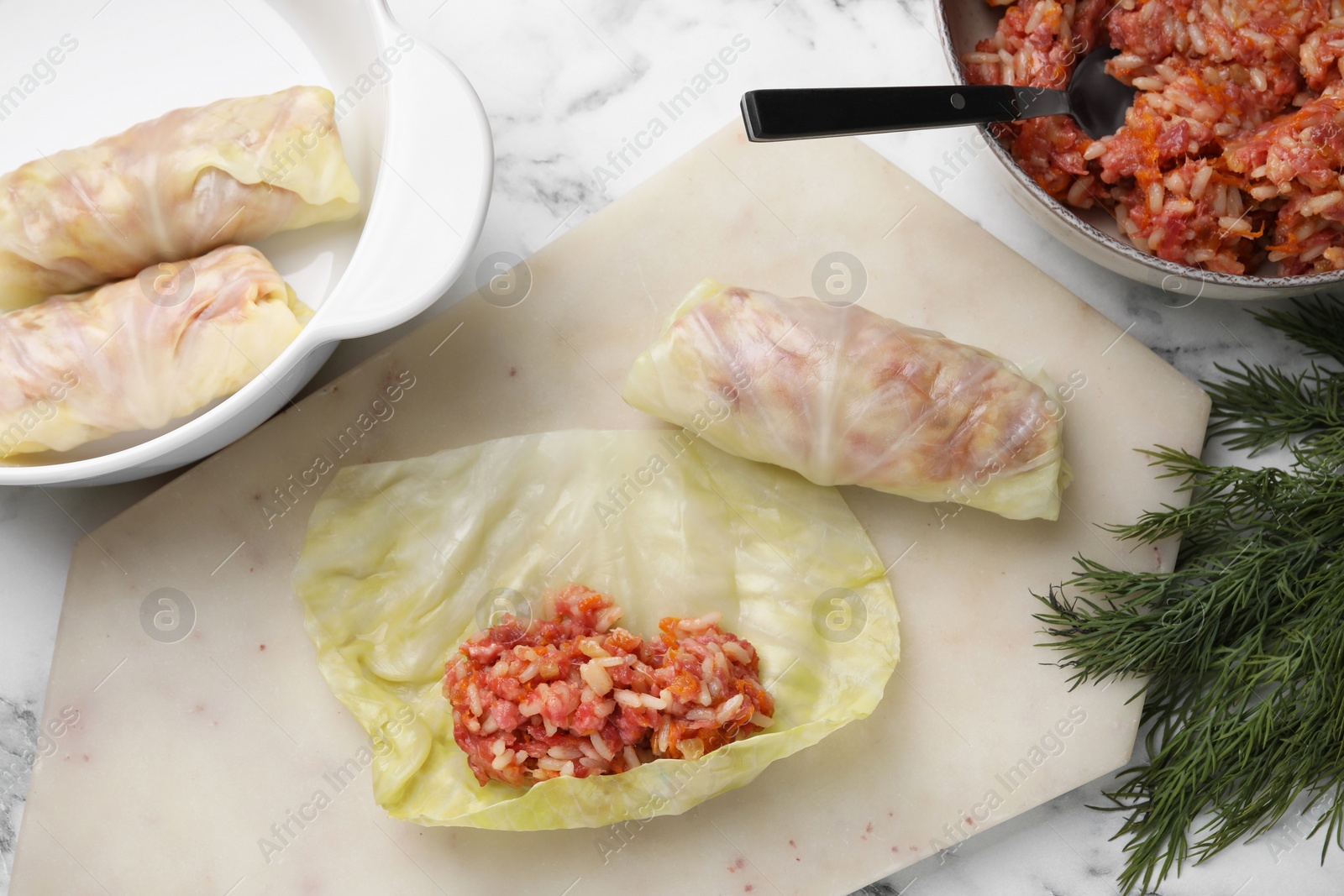 Photo of Preparing stuffed cabbage rolls on white marble table, flat lay