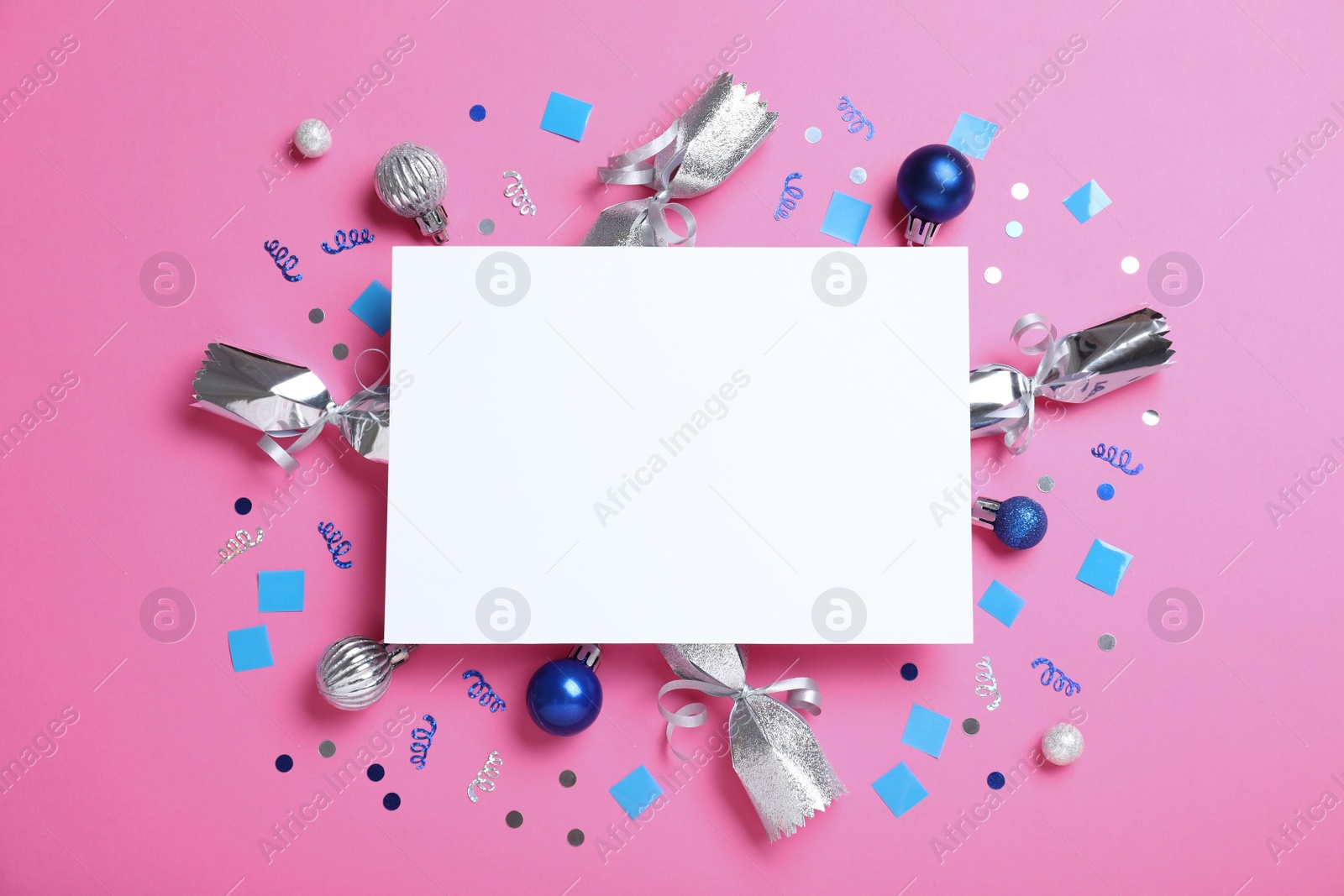 Photo of Flat lay composition of Christmas crackers, decorations, shiny confetti and blank paper on pink background. Space for text