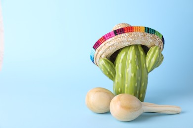 Photo of Wooden maracas and toy cactus with sombrero hat on light blue background, space for text. Musical instrument