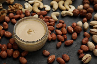 Delicious peanut butter and ingredients on black table, closeup