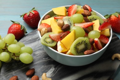 Photo of Tasty fruit salad in bowl and ingredients on table, closeup