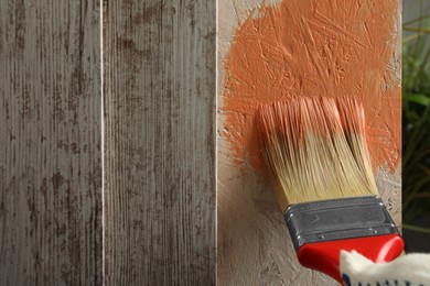 Worker applying coral paint onto wooden surface, closeup. Space for text