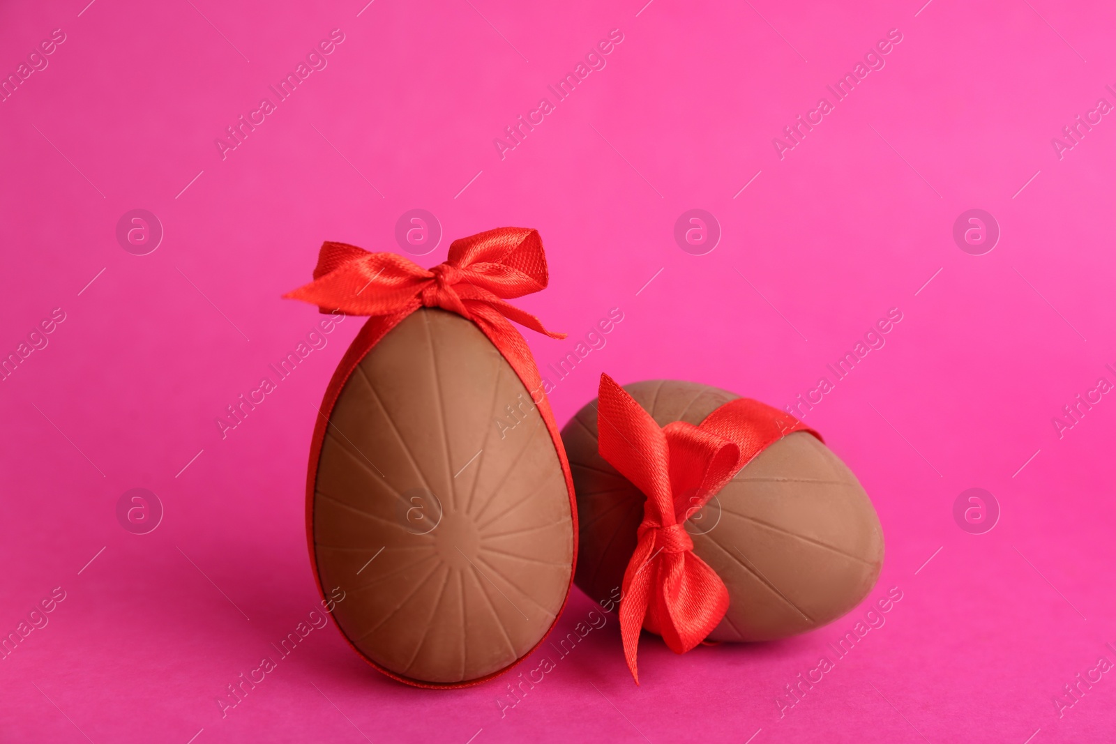 Photo of Sweet chocolate eggs with red bows on pink background