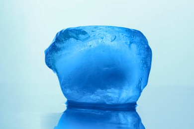 Photo of Crystal clear ice cube on light blue background, closeup. Color tone effect