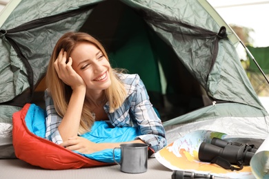 Photo of Young woman in sleeping bag looking outside of tent