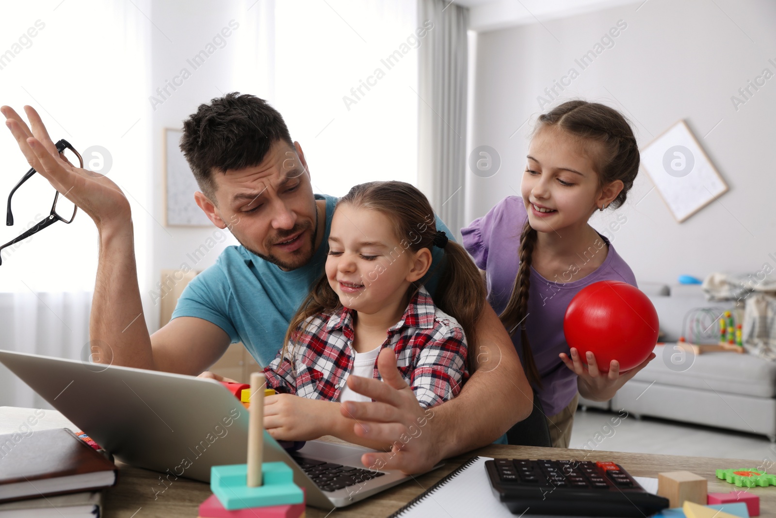 Photo of Children disturbing stressed man in living room. Working from home during quarantine