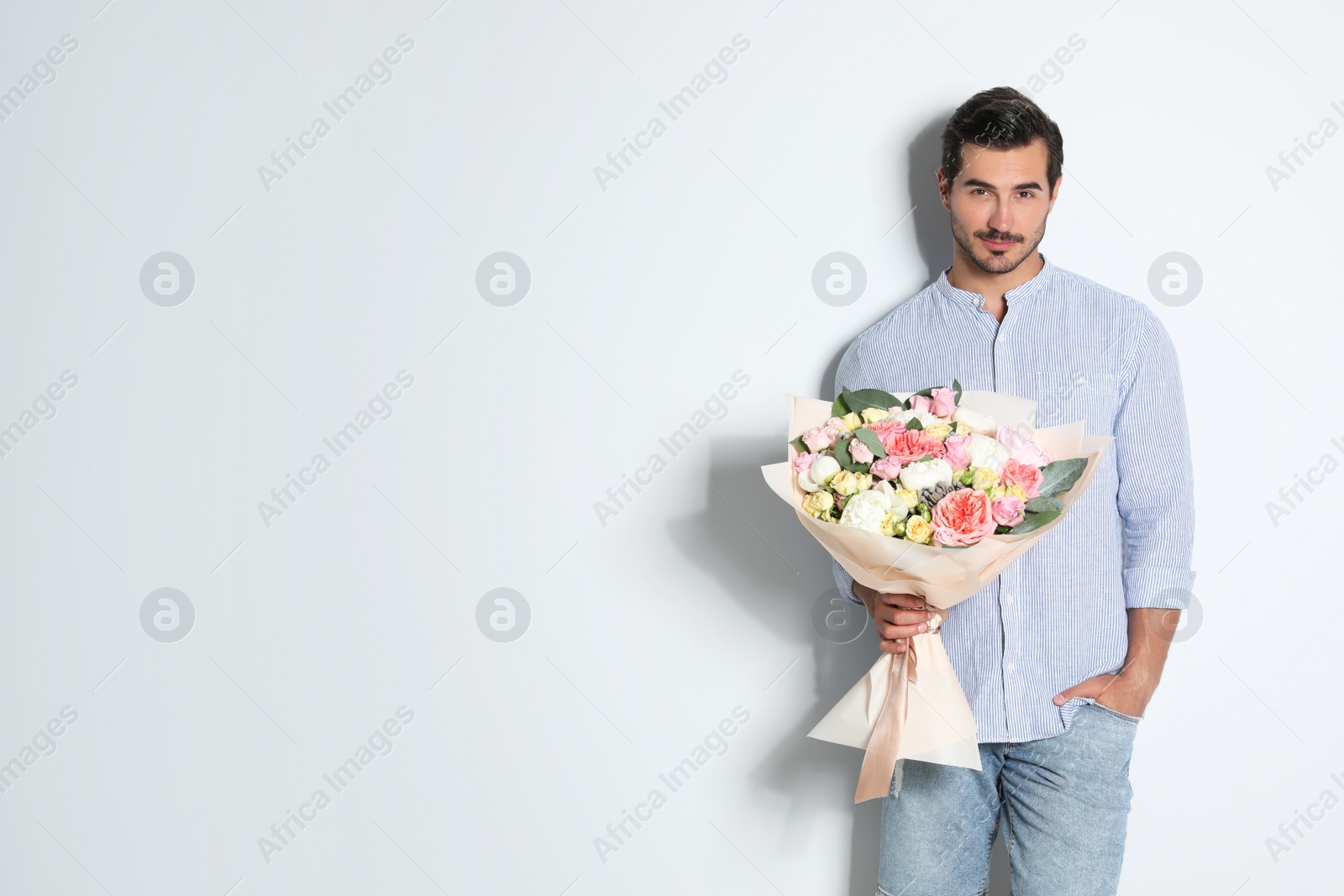 Photo of Young handsome man with beautiful flower bouquet on light background, space for text