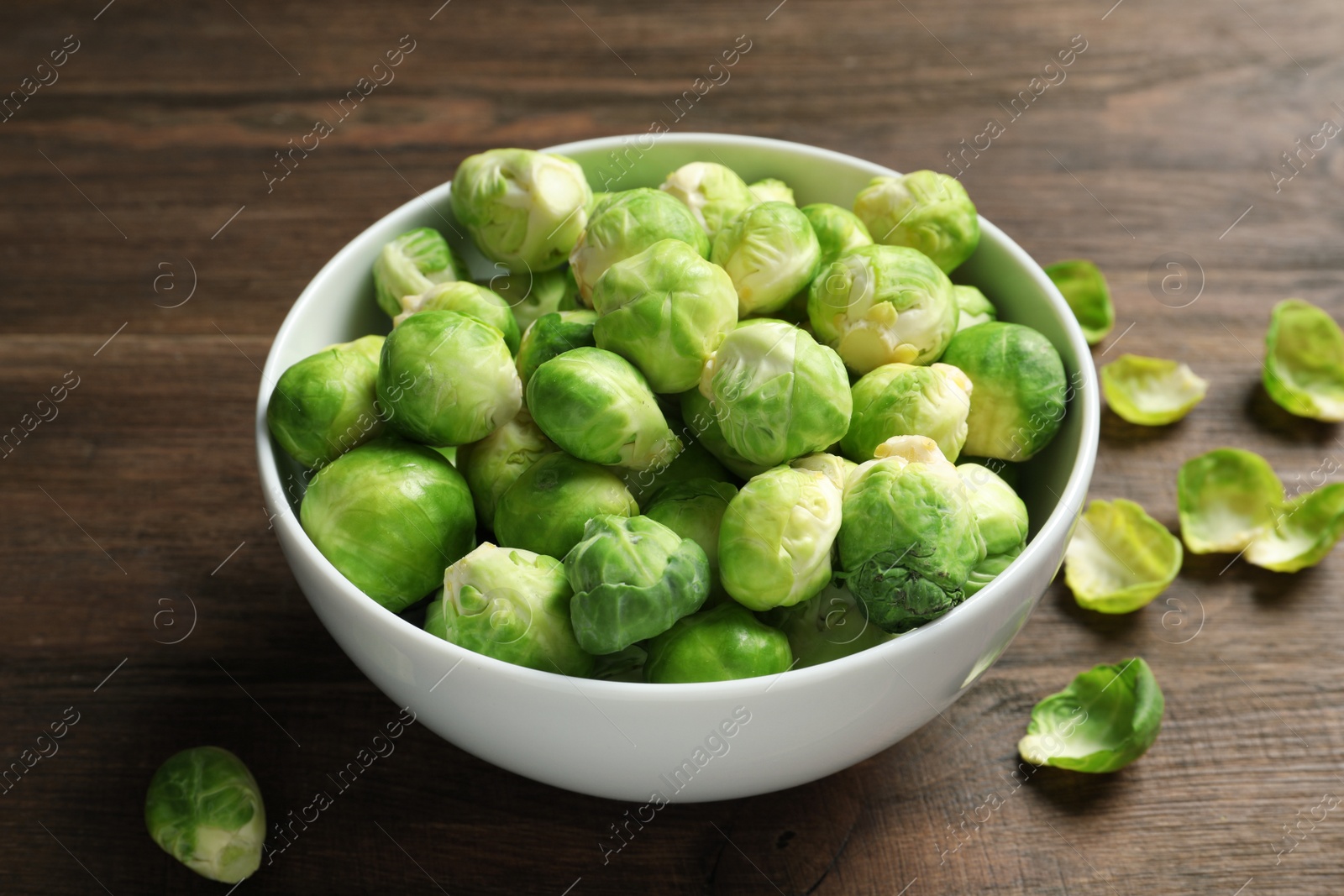 Photo of Bowl of fresh Brussels sprouts and leaves on wooden table