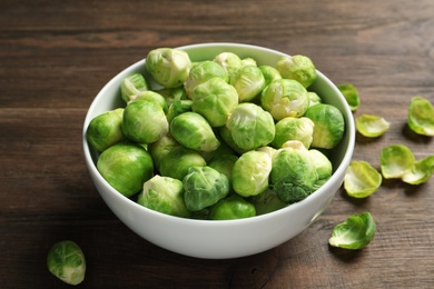 Bowl of fresh Brussels sprouts and leaves on wooden table