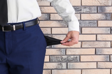 Photo of Businessman showing empty pocket near brick wall, closeup. Space for text