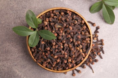 Photo of Aromatic cloves and green leaves in bowl on brown table, top view