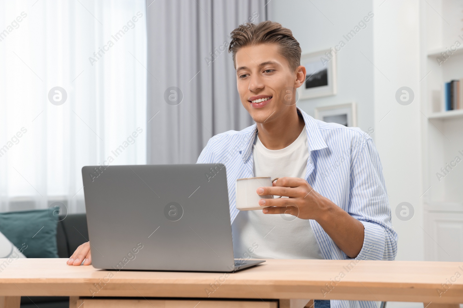 Photo of Happy young man having video chat via laptop at wooden table indoors