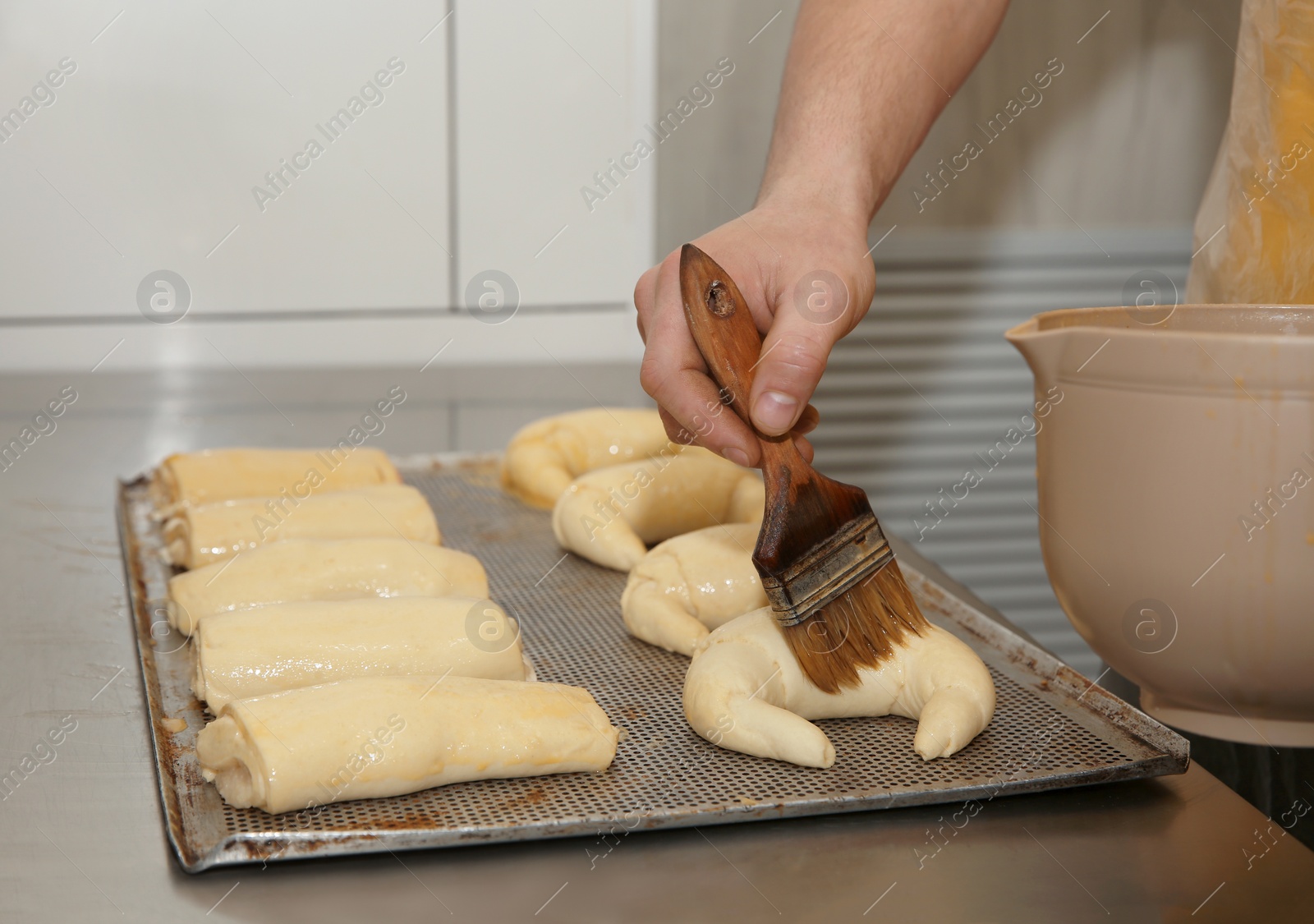 Photo of Baker covering pastries with egg white in workshop, closeup