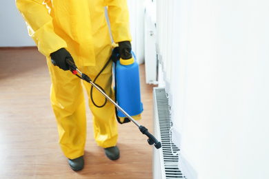 Photo of Pest control worker in protective suit spraying pesticide indoors, closeup. Space for text