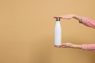 Photo of Woman holding thermos bottle on beige background, closeup. Space for text