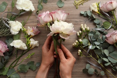 Florist creating beautiful bouquet at wooden table, top view