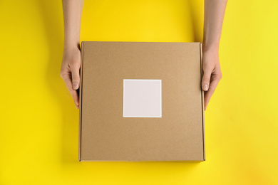 Woman holding cardboard box on yellow background, top view