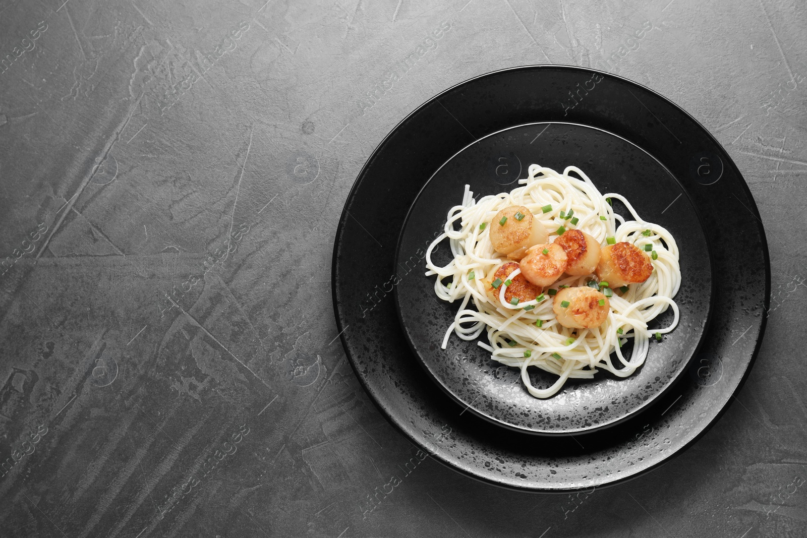 Photo of Delicious scallop pasta with green onion on grey table, top view. Space for text