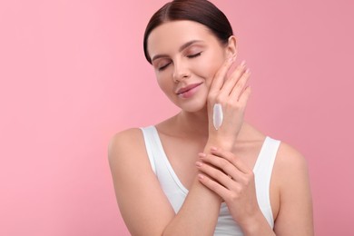 Beautiful woman with smear of body cream on her hand against pink background, space for text