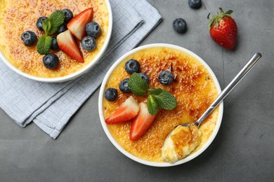 Delicious creme brulee with berries and mint in bowls on grey table, flat lay