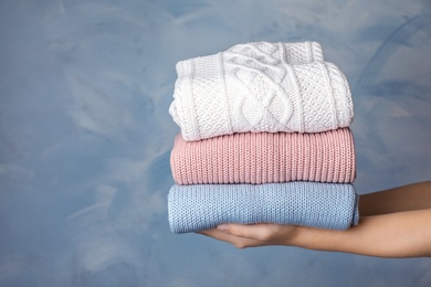 Photo of Woman holding stack of folded warm knitted sweaters against color background