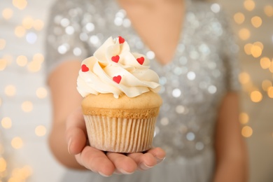 Woman holding tasty cupcake for Valentine's Day against blurred lights, closeup