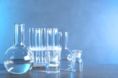 Photo of Laboratory glassware with liquid samples for analysis on grey table against toned blue background