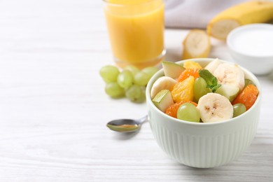 Photo of Delicious fresh fruit salad in bowl on white wooden table, space for text