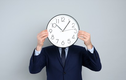 Businessman holding clock on grey background. Time management