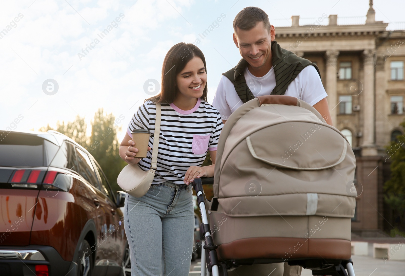 Photo of Happy parents walking with their baby in stroller outdoors