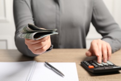 Photo of Money exchange. Woman holding dollar banknotes at wooden table, closeup