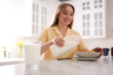 Photo of Woman with gallon bottle and breakfast cereal at white marble table in kitchen, focus on glass of milk