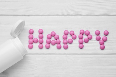 Word Happy made of pink antidepressants and medical jar on white wooden table, flat lay