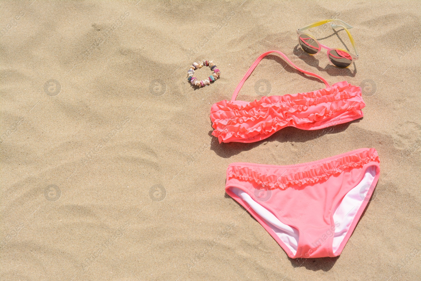 Photo of Sunglasses and bikini on sand, space for text. Beach accessories