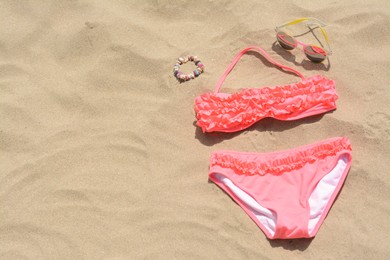 Photo of Sunglasses and bikini on sand, space for text. Beach accessories