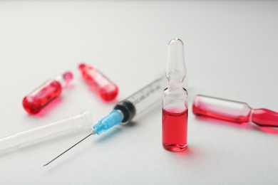 Photo of Glass ampoules with liquid and syringe on white background, closeup