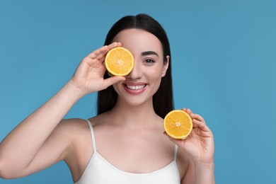 Photo of Beautiful young woman with pieces of orange on light blue background