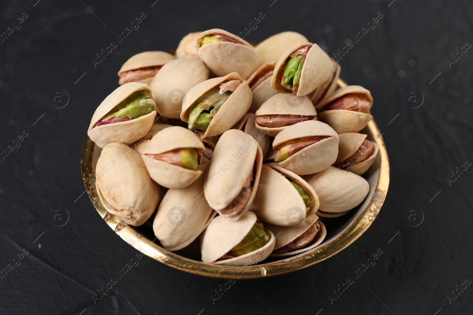 Photo of Tasty pistachios in bowl on black table, closeup