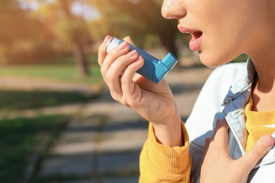 Photo of Woman using asthma inhaler outdoors. Space for text
