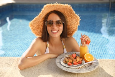 Photo of Young woman with delicious breakfast on tray in swimming pool