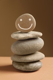 Photo of Stack of stones with drawn happy face on table against dark beige background. Zen concept