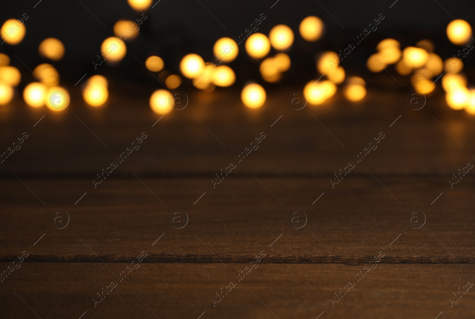 Photo of Blurred view of gold lights on wooden table, space for text