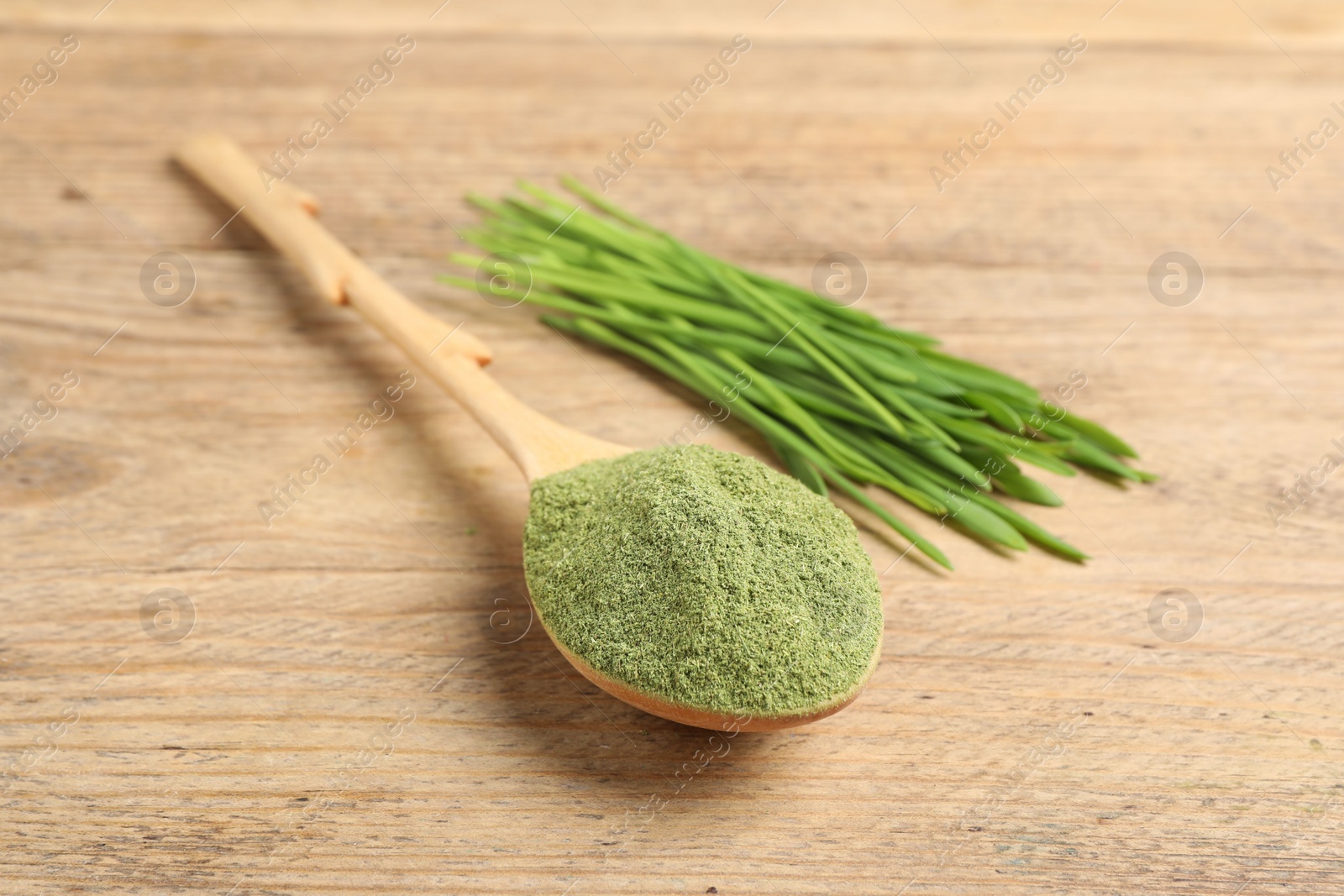 Photo of Wheat grass powder in spoon and fresh green sprouts on wooden table, closeup