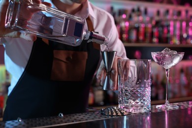 Cocktail making. Bartender pouring alcohol from bottle into jigger at counter in bar, closeup