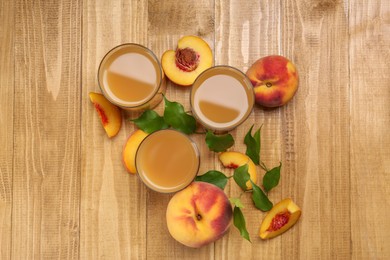 Photo of Glasses of peach juice, fresh fruits and leaves on wooden table, flat lay