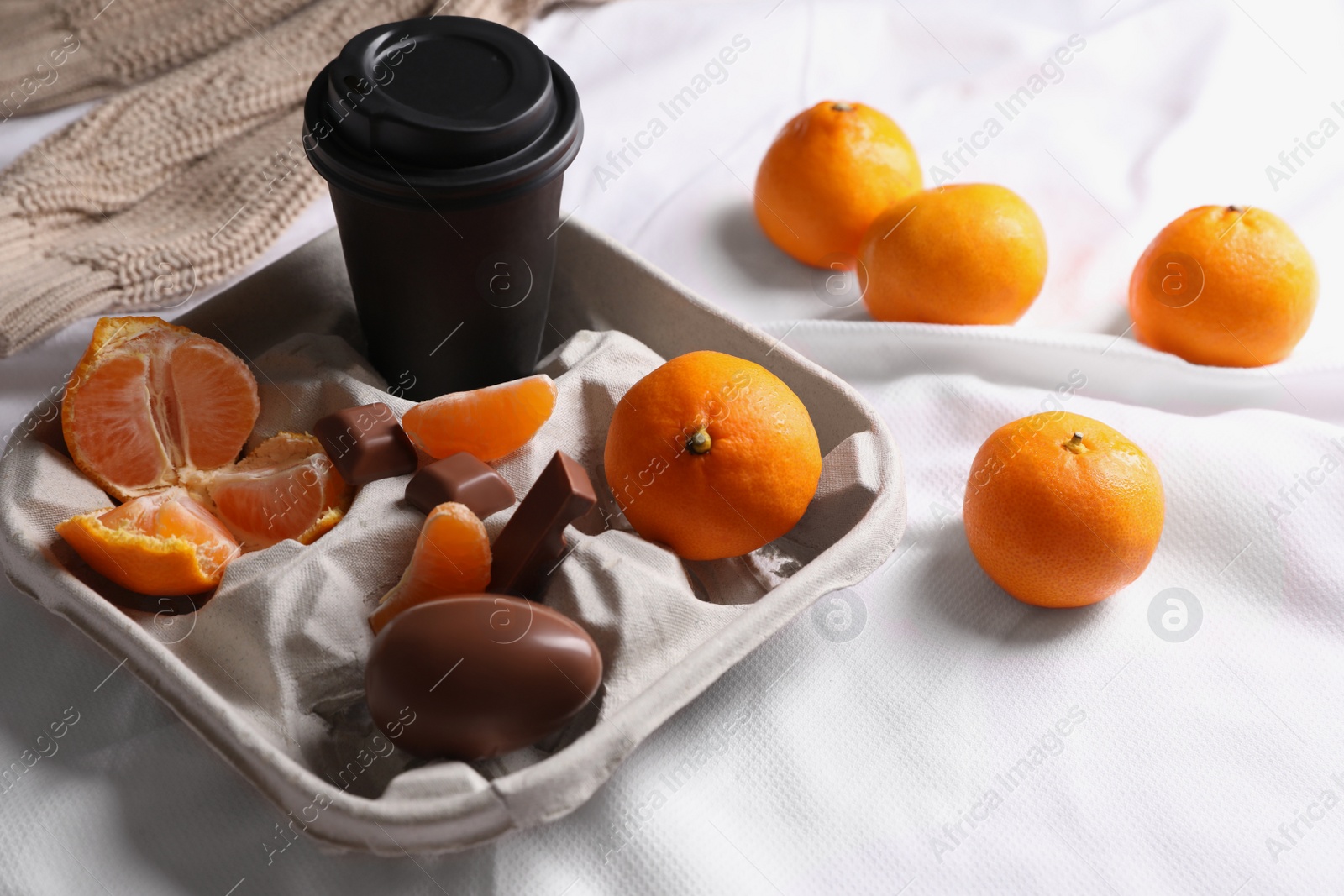 Photo of Delicious ripe tangerines, cup with drink and chocolates on white bedsheet